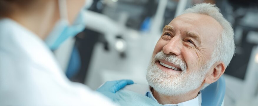 The elderly man smiling during a dental checkup with a caring professional.