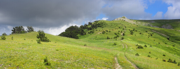 Panoramic view of a mountain plateau with green slopes and thunderclouds. Mountainous terrain of the highest peaks of the Crimean Mountains.