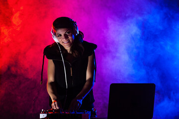 Female DJ playing music on a mixer. Red and blue lights and smoke in the background