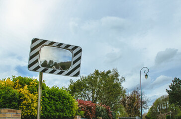Convex mirror installed for safe street visibility while driving near lush greenery on a clear day