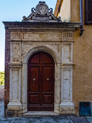 Arched wooden door within a carved stone doorway. Rich, dark red wood and detailed stone facade with elegance and architectural beauty. Travel to Siena, Tuscany, Italy,