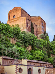 Basilica Cateriniana di San Domenico church rises above Siena, its imposing Gothic architecture framed from a low vantage point against the Tuscan sky. Travel in Italy.