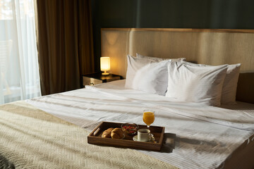 Fresh breakfast served on tray with croissants, coffee, and orange juice on neatly made hotel bed...