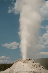 Castle Geyser erupting at yellowstone national park with fluffy clouds in sky