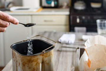 Man baking bread and sprinkle salt into the dough, closeup photo. Making bread dough at home with sugar and salt, spoon pouring ingredients into form