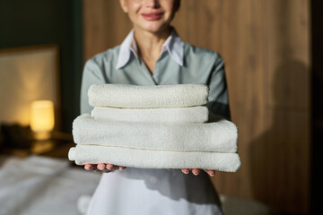 Plakat Portrait of smiling hotel attendant holding stack of fresh towels. Warm, inviting environment in background, suggesting welcoming service