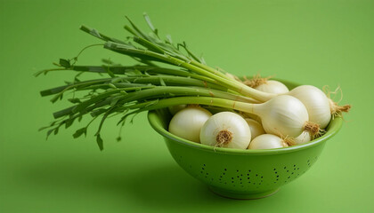 A green bowl filled with fresh white onions and their green stalks against a green background plain style