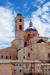 Urbino's cityscape features the magnificent Palazzo Ducale, a historic castle showcasing Renaissance architecture against a vibrant blue sky, inviting visitors to explore its rich heritage.