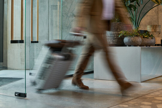 Business professional dragging luggage through sleek, contemporary hotel lobby with plants and design elements contributing to stylish environment