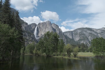 Scenery with granite cliffs, greenery, cascading waterfalls , puffy clouds and blue skies at...