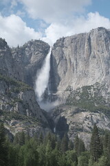 Scenery with granite cliffs, greenery, cascading waterfalls , puffy clouds and blue skies at...