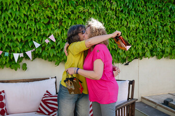 Two senior women embracing warmly with gift bags in hands during emotional moment of outdoor birthday celebration in decorated backyard