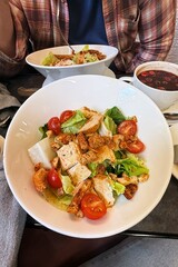 A white ceramic bowl with chicken and green leaf salad on a cafe table