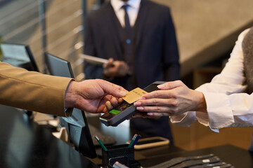 Two people engaging in payment exchange using credit card at reception counter. Focus on hands and card, with blurred background of suited individual