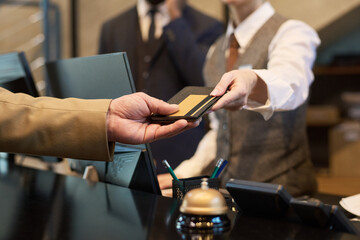 Fototapeta na wymiar Receptionist taking credit card from guest at hotel reception for transaction processing. Elegant setup with polished service tools like bell and pen holder visible on counter