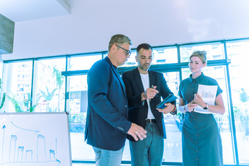 A group of business professionals reviews documents in a modern office, advises lawyers, and...