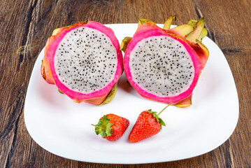 A pitahaya cut into two halves and two strawberries on a white plate.