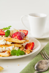 Belgian waffles with cottage cheese cream, strawberries, walnuts and mint on a white plate on a light table with a cup of coffee. Delicious, Sunday breakfast.