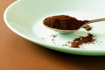 Spoon with ground coffee beans on plate on brown leather background, coffee