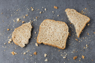 Slices of wholegrain wheat bread with crumbs on dark grey stone background. Toast bread pieces.