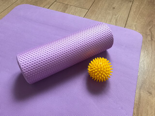 Sports equipment: purple myofascial release roller and yellow spiky ball on the background of yoga,...