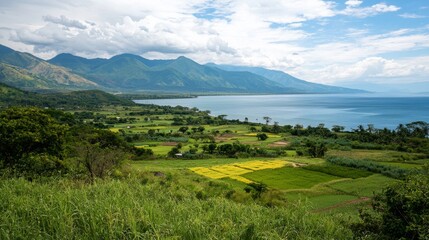 Expansive panoramic view of a large tranquil lake bordered by vibrant green agricultural fields and distant majestic mountains under a cloudy sky.