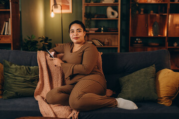 Obraz premium Cheerful African American woman spends time at home, chatting with friends via mobile phone