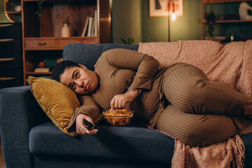 Obraz premium Plump female watches TV program with unhealthy snacks suffers from eating disorder