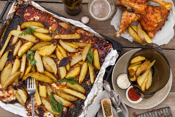 Top-down view of pub food: baked chicken drumsticks, rustic fries, sliced pickles, sauces, and beer. Cozy and casual atmosphere. Perfect for menus, blogs, or food delivery visuals