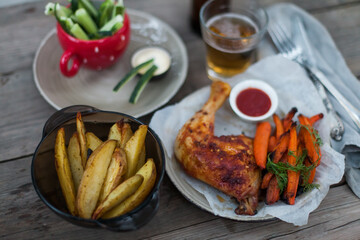 Top-down view of pub food: baked chicken drumsticks, rustic fries, sliced pickles, sauces, and beer. Cozy and casual atmosphere. Perfect for menus, blogs, or food delivery visuals