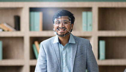 Fototapeta premium In a modern office, Indian guy smiles as facial recognition scans their face, showcasing the rise of advanced identification methods and our increasing reliance on technology.