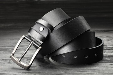 One black leather belt on wooden table, closeup