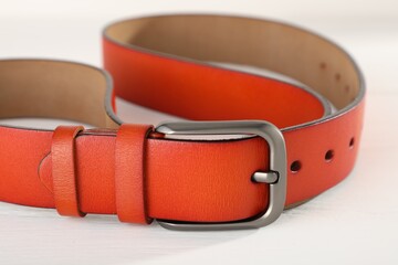 One orange leather belt on white wooden table, closeup