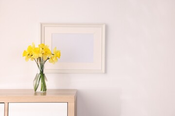 Beautiful daffodils in vase and picture frame on cabinet at home, space for text