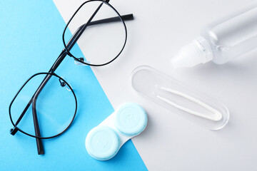 Case with contact lenses, glasses, tweezers and liquid solution on color background, flat lay