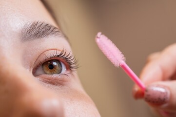 Caucasian woman brushing her eyelashes after lamination. 