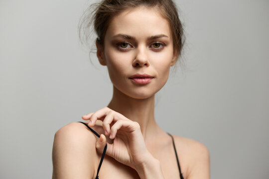 Elegant young woman with natural makeup, wearing a black top, posing with a gentle expression against a soft neutral background. Beauty and fashion concept.