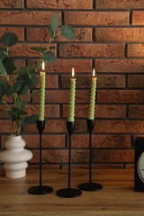 Candlesticks with burning candles on table near brick wall