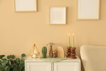Stylish candlesticks with burning candles and other decor on cabinet near beige wall indoors