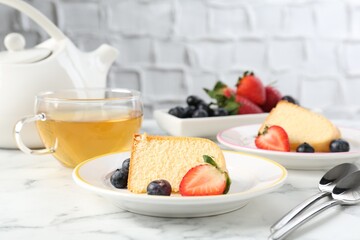 Pieces of tasty bundt cake with berries and tea on white marble table, closeup