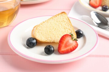 Tasty bundt cake with berries and tea on pink wooden table, closeup