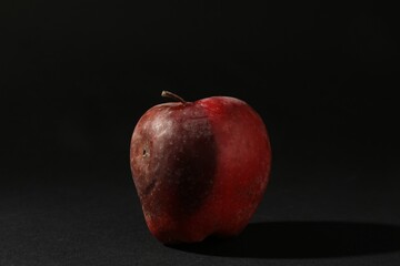 One rotten red apple on black background
