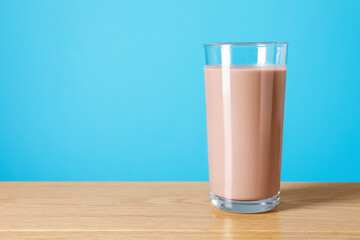 Tasty chocolate milk in glass on wooden table against light blue background, space for text