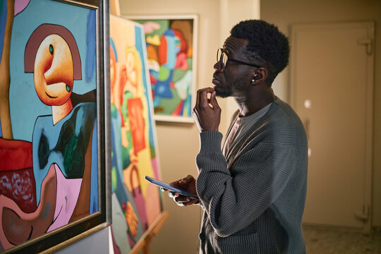 Individual examining an abstract painting in an art gallery. Holding a digital device, engaged in contemplation and study of the artwork, reflecting keen interest