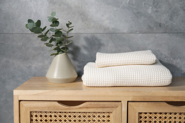 Waffle towels and vase with branches on wooden dresser near grey wall