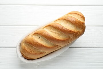 One bread loaf in basket on white wooden table, top view