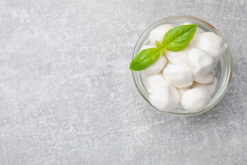 Mozzarella cheese balls and basil on light grey table, top view. Space for text