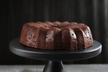 Tasty chocolate bundt cake on stand against blurred background, closeup