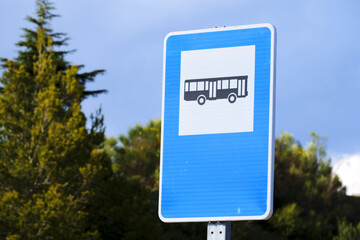 Blue bus stop sign against greenery and sky on sunny day
