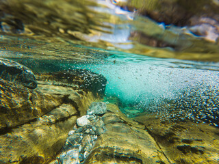 Mesmerizing underwater world of a cold Norwegian mountain river: crystal-clear water, stones, and air bubbles near the surface.